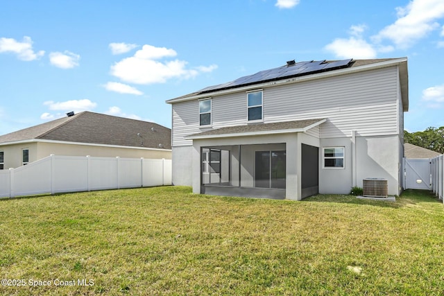 rear view of property with roof mounted solar panels, a fenced backyard, stucco siding, a lawn, and a sunroom