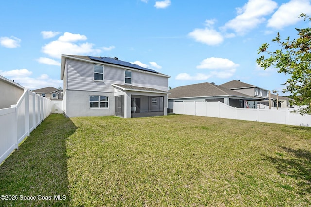 rear view of house featuring roof mounted solar panels, a fenced backyard, a sunroom, and a yard