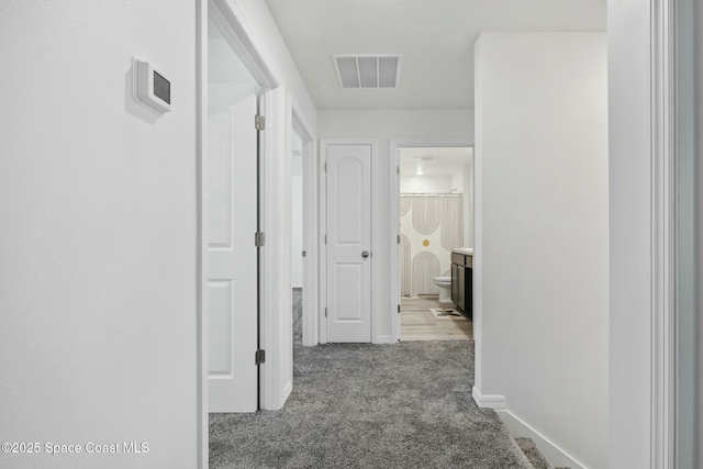 hallway featuring baseboards, visible vents, and carpet