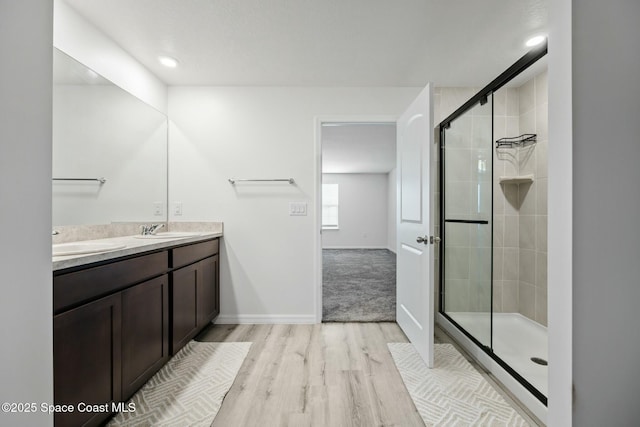bathroom with baseboards, wood finished floors, a stall shower, and a sink