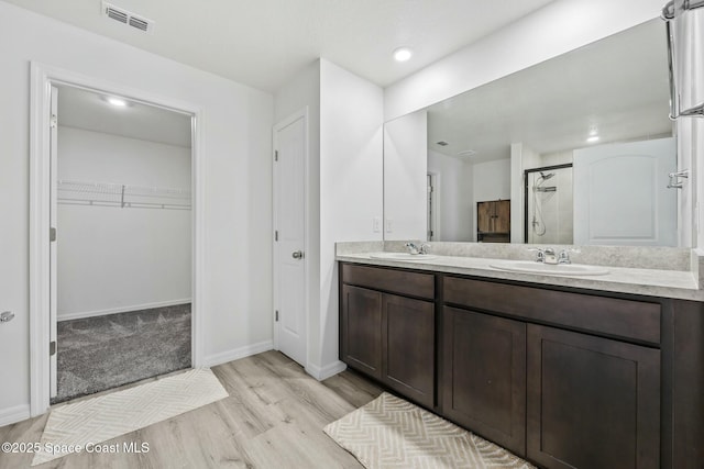 bathroom featuring wood finished floors, visible vents, tiled shower, and a sink