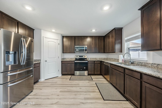 kitchen with light wood finished floors, dark brown cabinets, a sink, light stone countertops, and appliances with stainless steel finishes