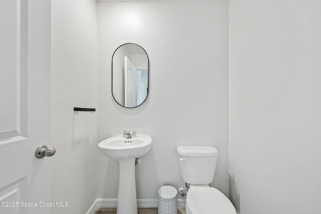 bathroom featuring toilet, baseboards, and a sink