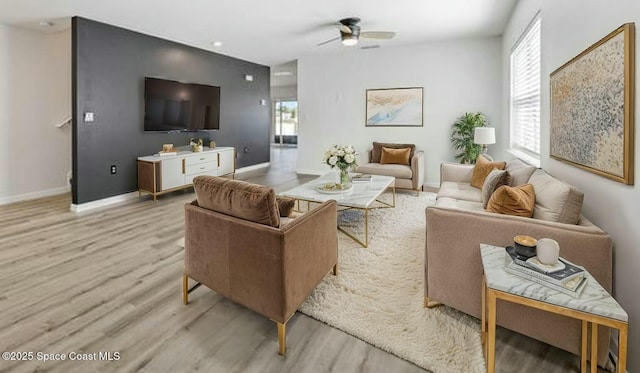 living area with a wealth of natural light, light wood finished floors, baseboards, and a ceiling fan
