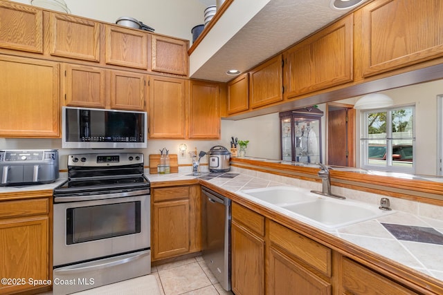 kitchen with light tile patterned floors, tile counters, a sink, and appliances with stainless steel finishes