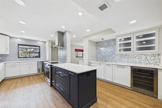 300 S Sykes Creek Pkwy Unit 106, Merritt Island, FL 32952 - kitchen with wall chimney range hood, appliances with stainless steel finishes, a center island, white cabinetry, and wine cooler
