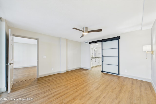 300 S Sykes Creek Pkwy Unit 106, Merritt Island, FL 32952 - unfurnished room featuring ceiling fan, a barn door, baseboards, and light wood-style floors