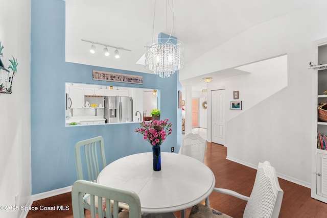 dining space featuring rail lighting, an inviting chandelier, dark wood-style floors, and baseboards