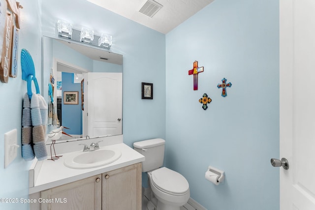 half bath featuring visible vents, baseboards, toilet, and vanity