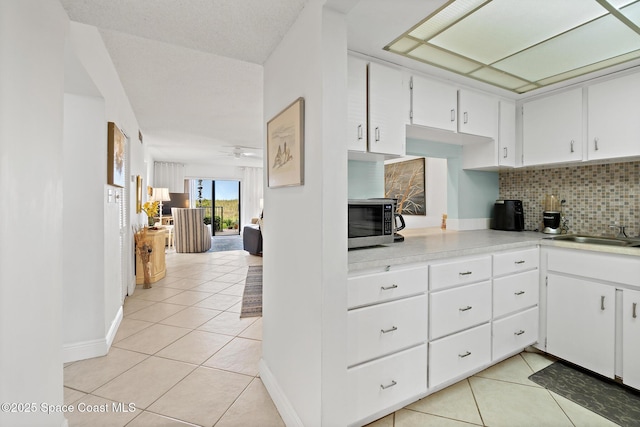 kitchen featuring tasteful backsplash, a sink, light countertops, stainless steel microwave, and light tile patterned flooring