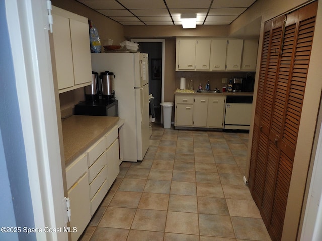 kitchen with white cabinets, a drop ceiling, light countertops, white appliances, and a sink