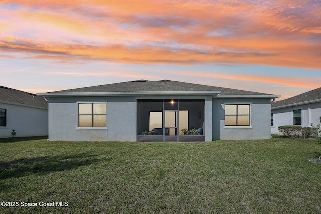 2241 Caravan Pl, Melbourne, FL 32940 - back of property at dusk with stucco siding, a lawn, and a sunroom