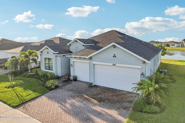 2241 Caravan Pl, Melbourne, FL 32940 - view of front of house with stucco siding, an attached garage, decorative driveway, a water view, and roof with shingles
