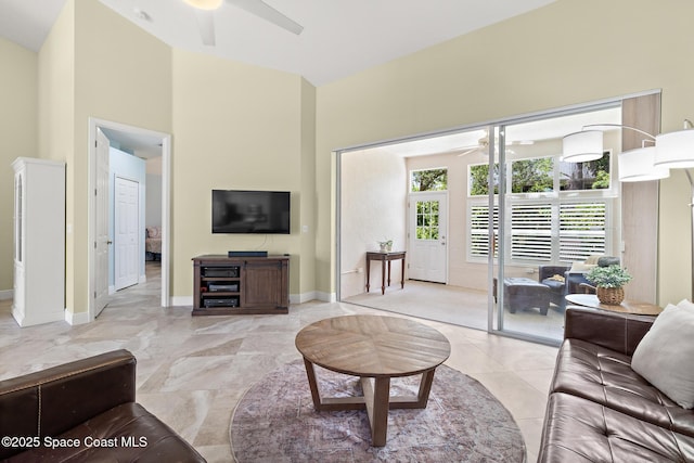 living area featuring baseboards, a ceiling fan, and a high ceiling