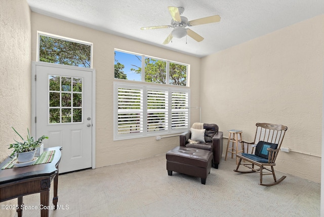 living area with a ceiling fan, a textured ceiling, and a textured wall