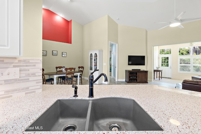 kitchen with decorative backsplash, light stone counters, a sink, baseboards, and high vaulted ceiling