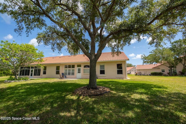 back of property with a lawn, stucco siding, and a tiled roof