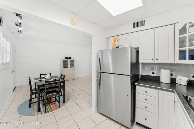 kitchen featuring freestanding refrigerator, dark countertops, white cabinetry, light tile patterned floors, and tile walls