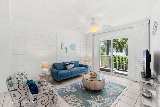 living area with a textured ceiling, tile patterned flooring, ceiling fan, and tile walls