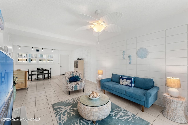 living room featuring light tile patterned floors, rail lighting, a ceiling fan, a textured ceiling, and tile walls