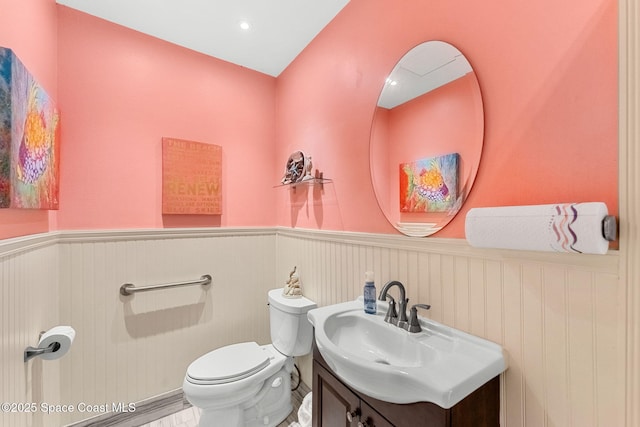 half bathroom with wainscoting, toilet, and vanity
