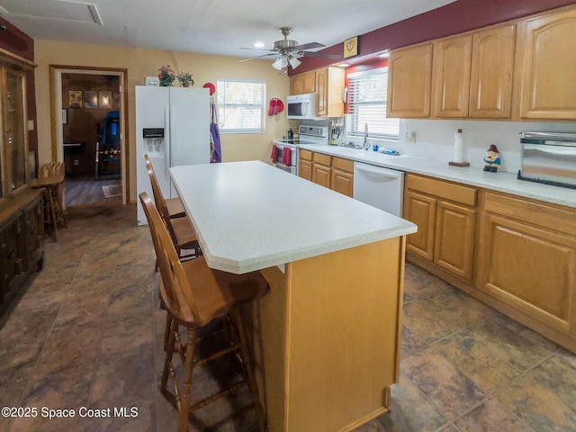 kitchen with white appliances, ceiling fan, light countertops, a kitchen island, and a breakfast bar area