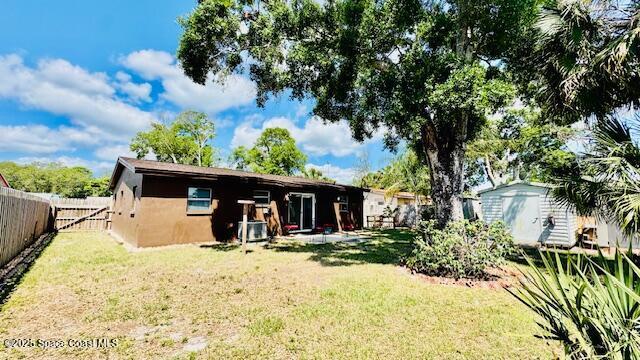 back of house with a fenced backyard, an outbuilding, a storage unit, and a lawn