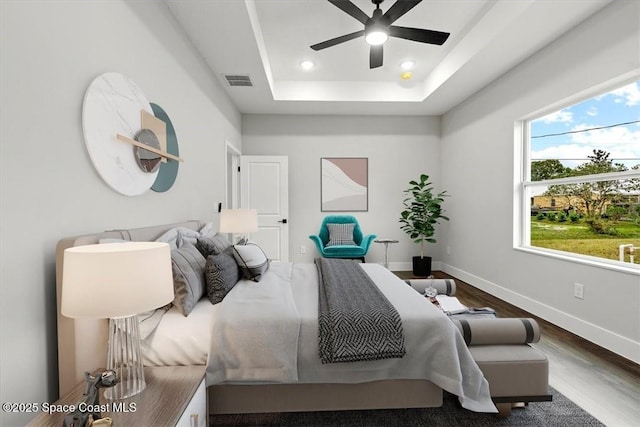 bedroom with recessed lighting, a raised ceiling, wood finished floors, visible vents, and baseboards