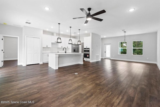 unfurnished living room with dark wood finished floors, visible vents, a ceiling fan, a sink, and baseboards