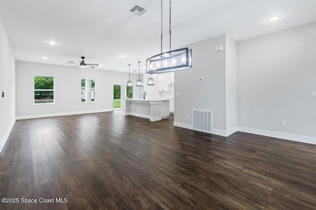 unfurnished living room featuring dark wood finished floors, visible vents, a ceiling fan, and baseboards