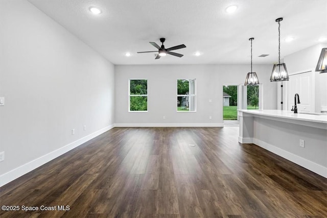 unfurnished living room with recessed lighting, dark wood finished floors, a sink, baseboards, and ceiling fan with notable chandelier