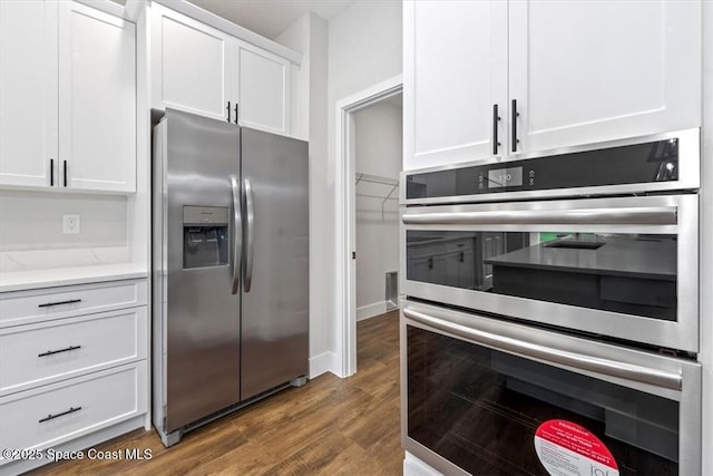 kitchen featuring white cabinets, baseboards, light stone counters, dark wood-type flooring, and appliances with stainless steel finishes
