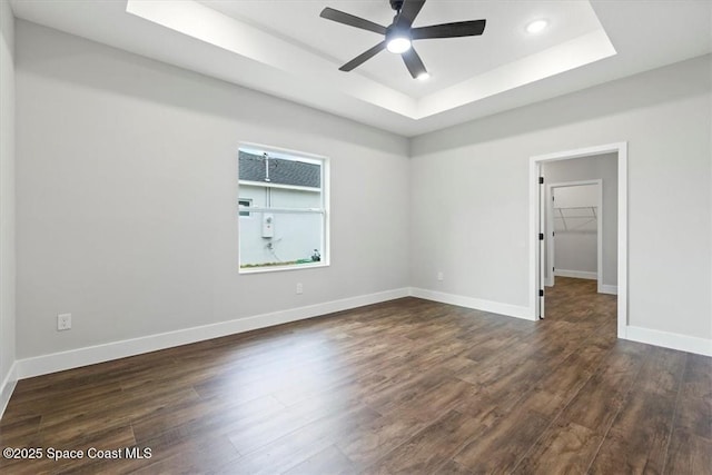 spare room featuring a ceiling fan, baseboards, dark wood-style flooring, and a raised ceiling