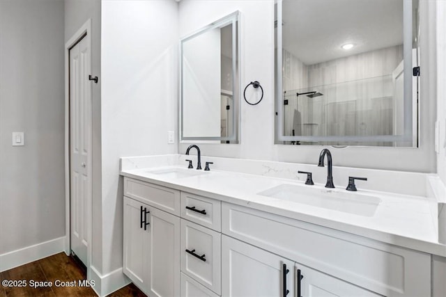 full bath with baseboards, a sink, double vanity, and tiled shower