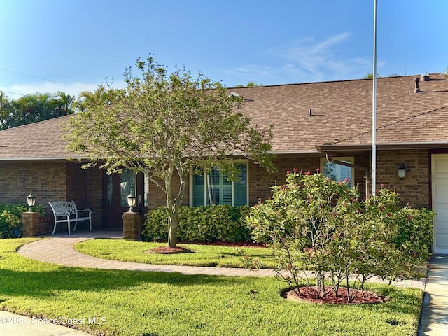 view of front of property featuring a front lawn, a shingled roof, and brick siding