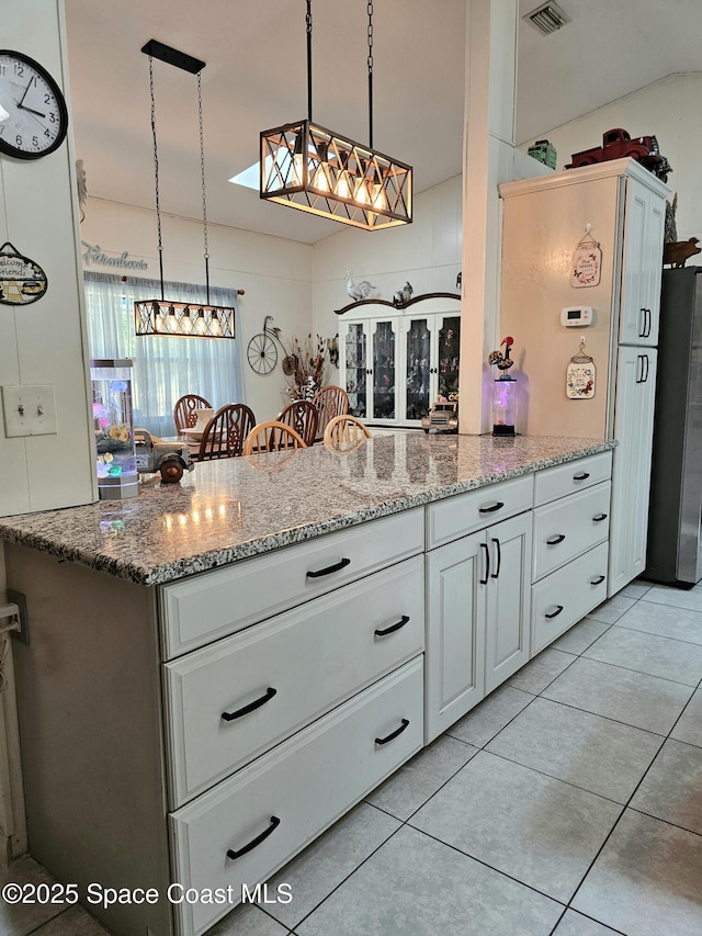 kitchen featuring freestanding refrigerator, light tile patterned flooring, a peninsula, light stone countertops, and white cabinets
