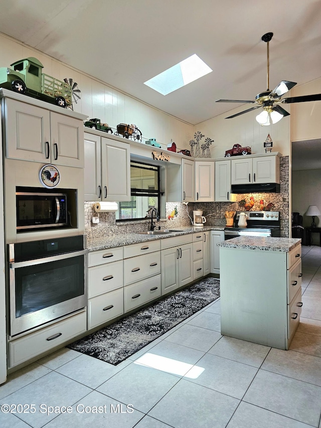 kitchen with stainless steel appliances, a skylight, a sink, under cabinet range hood, and decorative backsplash