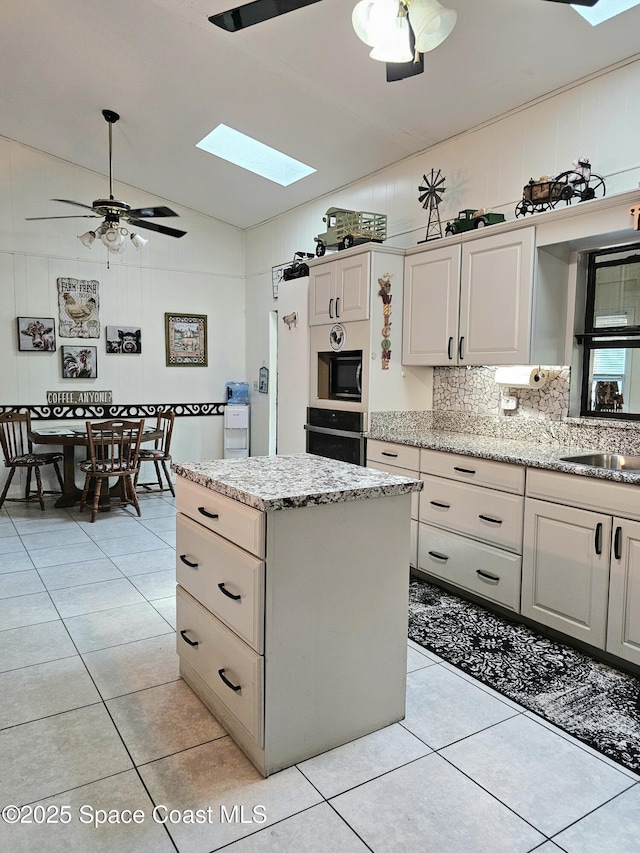 kitchen featuring a skylight, lofted ceiling, light tile patterned floors, black appliances, and a sink