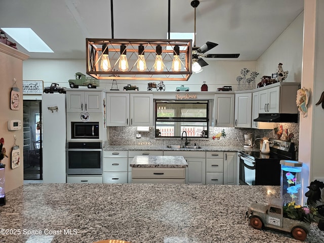 kitchen with appliances with stainless steel finishes, under cabinet range hood, a sink, a skylight, and backsplash