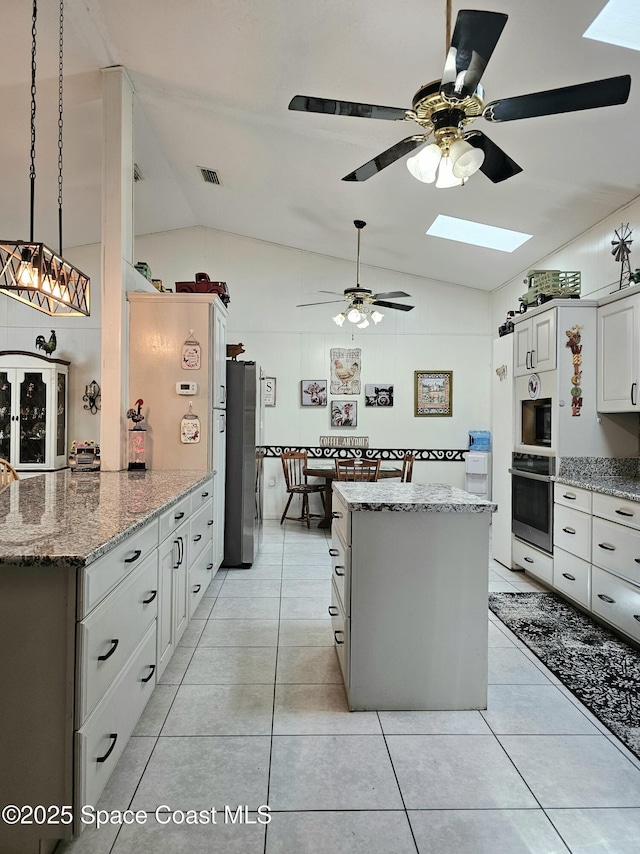 kitchen with vaulted ceiling, freestanding refrigerator, a skylight, ceiling fan, and a kitchen island