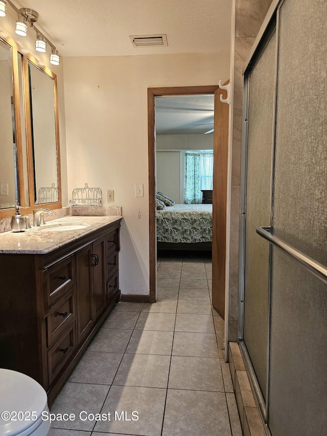 ensuite bathroom featuring tile patterned floors, a shower stall, vanity, baseboards, and toilet