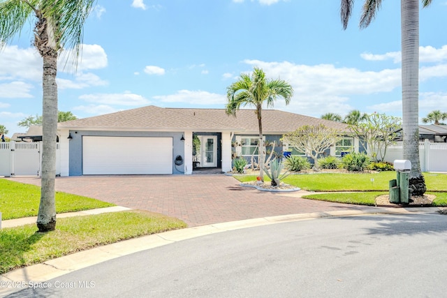 ranch-style house with a gate, a front lawn, stucco siding, an attached garage, and decorative driveway