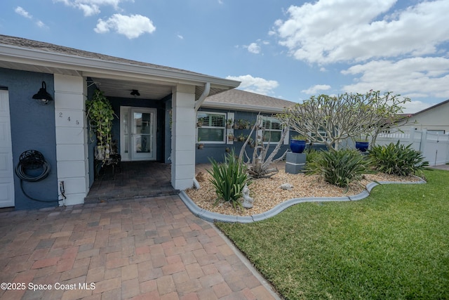 doorway to property with a lawn and a shingled roof