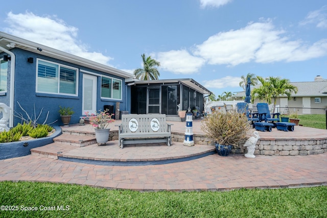 rear view of house with fence, stucco siding, a sunroom, and a patio