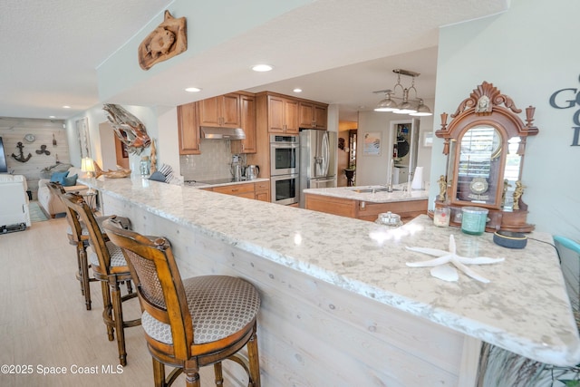 kitchen with stainless steel appliances, a peninsula, light stone counters, and a breakfast bar area