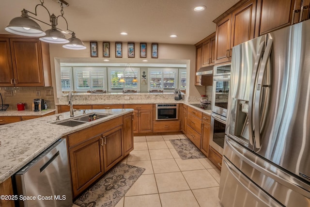 kitchen featuring brown cabinets, a sink, light stone countertops, tasteful backsplash, and appliances with stainless steel finishes