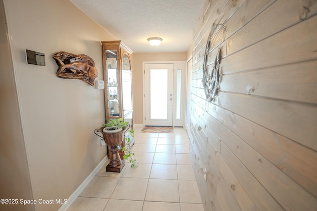 doorway to outside with baseboards, a textured ceiling, and light tile patterned floors