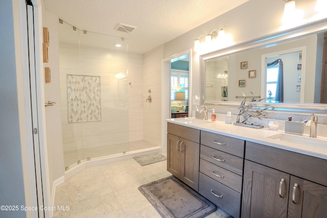full bath featuring a tile shower, double vanity, a textured ceiling, and a sink