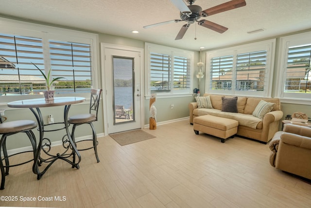 living area with ceiling fan, baseboards, a textured ceiling, and light wood-type flooring