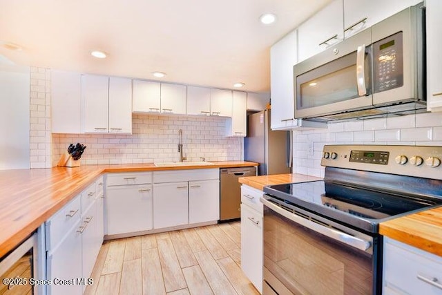 kitchen with butcher block countertops, white cabinets, appliances with stainless steel finishes, and a sink